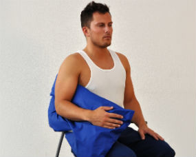 Mand sidder på stol med puden imellem arm og krop. Pude under underarm