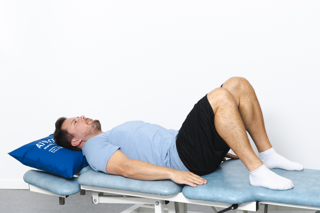 Patient udfører spænding af muskelkorsettet liggende på ryggen med bøjede ben
